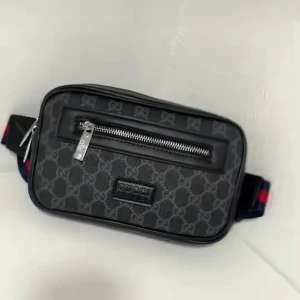 Svart Gucci axelväska med monogram - Snygg svart axelväska från Gucci med klassiskt GG-monogram och silverfärgade dragkedjor. Väskan har en justerbar rem i blått och rött samt praktiskt ytterfack med dragkedja. Perfekt för att bära det viktigaste med stil.