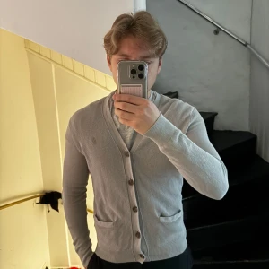 Grå kofta från Polo Ralph Lauren - Säljer en stilren grå kofta från Polo Ralph Lauren. Koftan har en v-ringad design med knappar framtill och två praktiska fickor. Perfekt för lager-på-lager under kyligare dagar. Sitter som S
