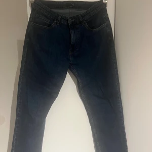 Mörkblå jeans från VRS Basis 32/32 - Snygga mörkblå jeans från VRS Basis i klassisk femficksmodell. Jeansen har raka ben, normal passform och är tillverkade i slitstarkt denimtyg. Perfekta för dig som gillar en enkel och stilren look. Storlek 32/32.