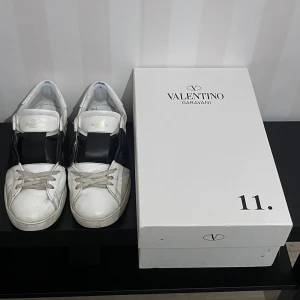 Valentino Garavani Open sneakers vit/svart - Snygga Valentino Garavani Open skor i vitt skinn med svart band över mitten. Perfekta för dig som gillar exklusiva och trendiga skor. Rätt så använda som man kanske kan se men fortfarande rätt så bra skick. Sulan är lite nerslipad som man kan se på grund av lång användning. Annars är de bara en liten skada som knappt syns på sista bilden. Bara höra av er om ni har någon fråga mvh Liam.