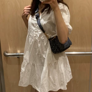 Vit kort klänning från Zara - Supersöt vit kort klänning från Zara med volangdetaljer och lätt puffade korta ärmar. Klänningen har en avslappnad passform och är gjord i bomull, perfekt för varma dagar. Enkel och stilren design som är lätt att matcha med accessoarer.