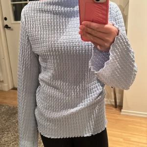 Ljusblå långärmad topp med vågig struktur - Supersnygg ljusblå långärmad topp med vågig, texturerad yta och lätt utsvängda ärmslut. Materialet är mjukt och stretchigt, perfekt för dig som gillar unika detaljer.💗Vet ej märke eller storlek då lappen i tröjan är borta men passar XS-S