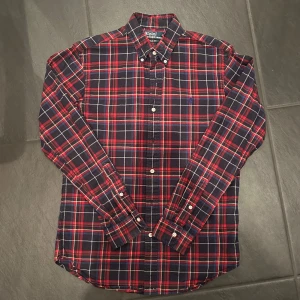 Rutig skjorta från Polo Ralph Lauren - Riktigt snygg rutig skjorta från Polo Ralph Lauren i slim fit. Skjortan är mörkblå med röda och vita rutor, har långa ärmar och klassisk krage. Broderad logga på bröstet och knäppning framtill. Perfekt för dig som gillar preppy stil.