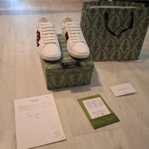 Gucci Ace sneakers med orm - Säljer ett par vita Gucci Ace sneakers i skinn med broderad röd och svart orm på sidan samt klassiska gröna och röda ränder. Skorna har snörning, rund tå och detaljer i rött och grönt på hälen. Kommer med originalkartong, dustbag och kvitto. Priset är diskuterbart 😀