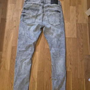 Ljusgrå skinny jeans med slitningar - Säljer ett par ljusgrå skinny jeans med slitna detaljer på framsidan. Jeansen har en tvättad look och klassiska bakfickor. Perfekta för dig som gillar en trendig och avslappnad stil.