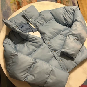 Ljusblå pufferjacka från Alo - Alo Yoga Glacier Puffer Jacket – supervarm och stilren dunjacka i en ljusblå färg 💙 Jackan är helt ny med taggar, aldrig använd. Köpt via Vinted, så jag har inget kvitto, men skicket är perfekt. Mycket hög kvalitet – lätt men håller värmen otroligt bra.  Storlek: M Om ingen köper den snart planerar jag att börja använda den själv… så passa på innan dess 😉