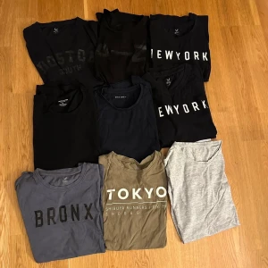 10-pack t-shirts med tryck och basic - Säljer ett paket med t-shirts i olika färger och tryck, bland annat med texten NEW YORK, TOKYO, BOSTON och BRONX. Färgerna är svart, grå, blå, olivgrön och ljusgrå. Alla är kortärmade och i mjuk bomull, vissa med rund hals och enkla tryck framtill. Har AZ tröja och Jack N Jones tröja också.