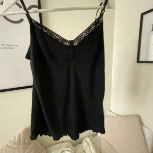 Svart linnetopp med spetsdetalj Calvin Klein - Snygg svart linnetopp med tunna axelband och spetsdetalj vid halsringningen. Strl M men passar S/XS