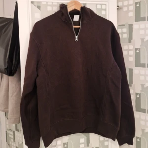 Brun sweatshirt med half zip från Zara - Mörkbrun sweatshirt med half zip och hög krage. Tröjan har långärmade ärmar och är tillverkad i mjukt bomullsmaterial. Enkel och clean design utan tryck eller mönster, perfekt för chill dagar.