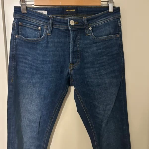 Blå jeans från Jack & Jones - Säljer ett par klassiska blå jeans från Jack & Jones med snygga kontrastsömmar och femficksdesign. Jeansen har normal passform och raka ben, tillverkade i mjukt denimtyg. Perfekta för en avslappnad och stilren look.