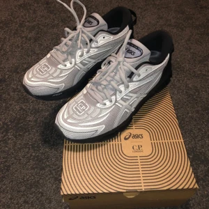 ASICS x C.P. Company Gel-Quantum 360 - Snygga ASICS Gel-Quantum 360 sneakers i samarbete med C.P. Company. Skorna har en futuristisk design i ljusgrått och svart med vita detaljer, mesh-överdel och tydlig logga på tån och hälen. Platt sula med FF Blast+ teknologi och snörning för perfekt passform.