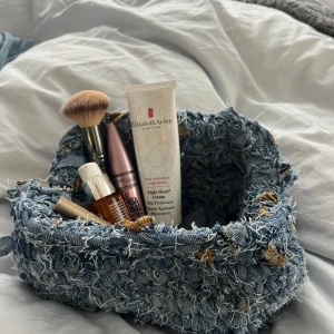 Handväska i återvunnen denim - Unik handväska virkad av återvunna denimtyger i olika blå nyanser. Väskan har en cool, ruffig look med fransiga detaljer och inslag av bruna toner. Perfekt för dig som gillar statement-accessoarer och vill sticka ut med en kreativ och hållbar stil.