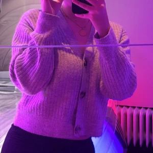 Ljusgrå ribbad kofta med knappar - Supermysig ljusgrå kofta med ribbad struktur och stora knappar framtill. Croppad modell med lång ärm och v-ringad hals. Perfekt att slänga på sig när det är kyligt ute.