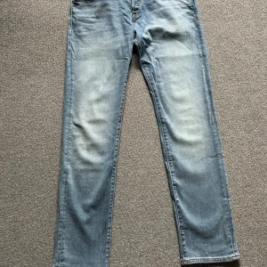 Ljusblå jeans från Jack & Jones - Säljer ett par ljusblå jeans från Jack & Jones med klassisk femficksdesign och snygga slitningar framtill. Jeansen har raka ben och subtila detaljer på bakfickorna. Tillverkade i bomull för en skön känsla och avslappnad look.