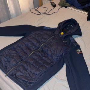 Mörkblå pufferjacka Parajumpers L - Snygg mörkblå pufferjacka från Parajumpers med huva och coolt patch på ärmen. Jackan har quiltad framsida och rygg, dragkedja hela vägen samt praktisk bröstficka med zip. Materialmix av polyester och syntet, perfekt för kyliga dagar. Pris kan diskuteras men nypriset ligger på 3500 