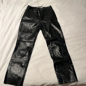 Svarta byxor i skinnlook Carin Wester - Snygga svarta byxor från Carin Wester i glansig skinnlook med croco-mönstrad yta. Byxorna är raka i modellen och tillverkade i 100% polyuretan. 