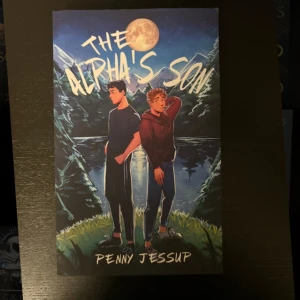 The Alpha's Son - En ungdomlig roman med två unga personer vid en sjö under fullmånen. Perfekt för dig som gillar spänning, relationer och mystik i en modern miljö. Omslaget har en tecknad stil som lockar unga vuxna.