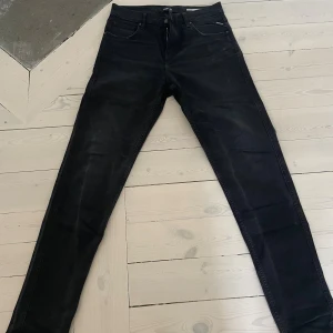 Svarta Replay jeans Sandot 30/34 - Svarta jeans från Replay, modell Sandot, med relaxed tapered fit. Klassisk femficksdesign, dragkedjegylf och diskreta Replay-detaljer. Jeansen är i stretchigt denimtyg och har en snygg, mörk tvätt som passar till allt.