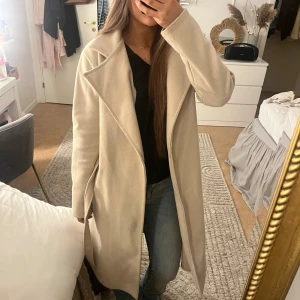 Beige kappa med bälte - Säljer en beige kappa som är ifrån missay, med ett bälte i midjan. Perfekt för dig som vill ha en snygg jacka till höst och vår. Jackan är lite nopprig då jag köpte den i somras och då den har andvändts under sommaren🫶