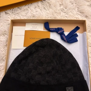 Louis vuitton mössa petit damer  - Exklusiv mörkgrå mössa från Louis Vuitton med diskret rutigt mönster och LV-logga framtill. Mössan är tillverkad i mjuk ull och har en bred ribbad kant för extra komfort. Perfekt accessoar för dig som vill ha en lyxig och stilren look. Petit Damer OG lv mössa, kommer med kartong och allt medföljer som är i bilden. 100% äkta! 