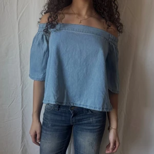 Offshoulder denimtop med öppen rygg - Ljusblå offshoulder topp i denim. Öppen rygg med resår. Perfekt för en trendig denim look nu till hösten.