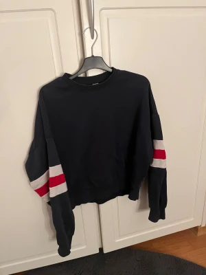 Blå tröja -  Blå tröja ifrån H&M i storlek XS med röda och vita ränder på armarna