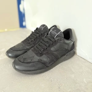 Svarta Valentino Garavani Rockrunner - Snygga svarta Valentino Garavani Rockrunner sneakers med coola camouflagedetaljer. Skorna har en mix av skinn och mocka, rund tå och klassisk snörning. Perfekta för dig som gillar en stilren men edgy look. Det ingår box och en Valentina dustbag!😊