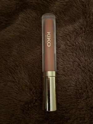 KIKO Milano nude läppglans - Säljer ett nude-färgat läppglans från KIKO Milano. Tuben har frostat plast och ett snyggt guldfärgat lock som ger en lyxig känsla. Perfekt för dig som gillar naturliga och mjuka färger på läpparna.