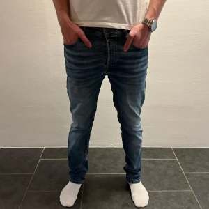 Jack & Jones Slim Straight jeans blå - W31 L32. Snygga blå jeans från Jack & Jones i modellen Slim Straight Tim. Jeansen har klassisk femficksdesign, normal midja och raka ben med en slim passform. Tillverkade i mjukt denimtyg med snygga slitningar och ljus tvätt. Perfekta för en avslappnad och stilren look.