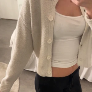 Beige stickad kofta med knappar - Mysig beige stickad kofta från Cubus med rund hals och fem stora vita knappar framtill. Koftan har ribbade muddar vid ärmslut och nederkant, samt en loose passform som ger en chill vibe. Perfekt att slänga över en topp för extra lager.