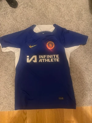 Chelsea Tröja  - Blå Chelsea fotbollströja med Infinite Athlete tryck och Nike logga. 