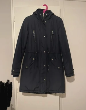 Mörkblå Parkajacka Vinterjacka - Mörkblå Vinterjacka från Vero Moda för damer i nyskick. Värmer otroligt bra och är bekväm. Borttagbar päls från huvan & fyra fickor på utsidan barav två har dragkejdor (se bild). Har både knappar och dragkedja. Storlek 38/M