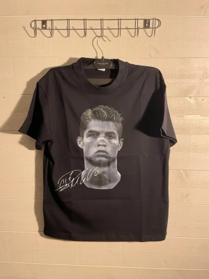 Svart t-shirt med tryck från Selected - Svart t-shirt från Selected med stor grafisk print framtill av ett porträtt och signatur, samt en stor grå och vit logga med text på ryggen. Klassisk passform och rund hals. Materialet känns mjukt och skönt, perfekt till jeans eller shorts.