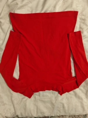 Röd offshoulder topp - Säljer en snygg röd offshoulder topp med lång ärm. Toppen har en tight passform och är tillverkad i mjuk bomull som sitter skönt mot kroppen. Perfekt för dig som vill ha en enkel men stilren look med en poppande färg.