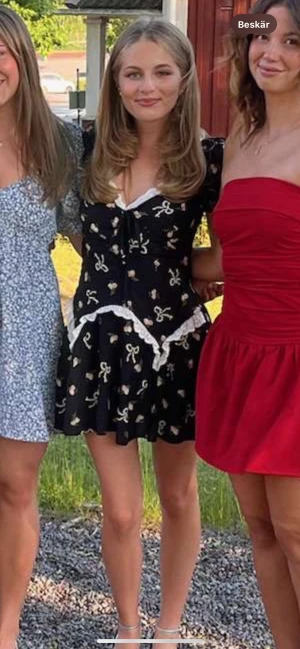 Svart blommig kortklänning med spets - Supersöt svart kortklänning med puffärmar, vita spetsdetaljer och blommigt mönster med små rosa rosor och rosetter. Klänningen har en v-ringad hals med snörning framtill och en flowy kjol. Har endast använt en gång (inga tecken på användning). Köpte den på asos runt 500kr