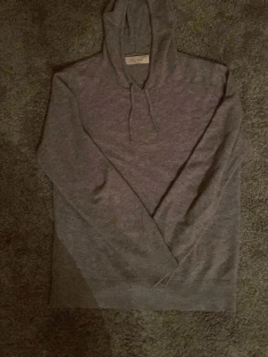 Grå Kashmir hoodie från Sayless - Mjuk och stilren grå hoodie från Sayless i kashmir. Klassisk modell med huva och dragsnören, ribbade muddar och lång ärm. Perfekt för dig som gillar en clean och enkel look