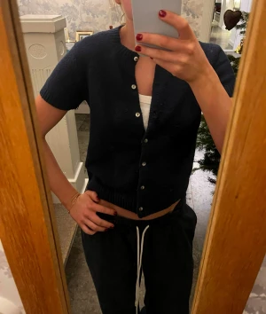 Mörkblå kofta från Kimchi Blue XS - Kortärmad mörkblå kofta från Kimchi Blue i storlek XS. Tröjan har rund hals, knappar framtill och ribbade muddar vid ärmslut och nederkant. Perfekt att slänga på över ett linne för en chill look.