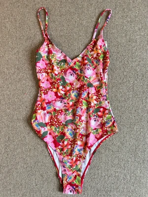 Röd blommig baddräkt Beck Söndergaard - Färgstark baddräkt från Beck Söndergaard i modellen Salsa Red. Den har tunna axelband och ett blommigt mönster i rosa, grönt, lila och orange på röd botten. Tillverkad i återvunnen polyester, perfekt för dig som gillar att sticka ut på stranden.