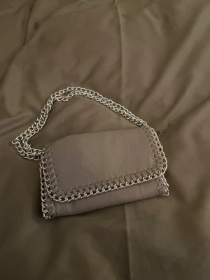 Beige axelväska - Säljer en ljusgrå axelväska med silverfärgad kedja. Går att ha som axelväska samt crossbody. Skriv för fler bilder🩷