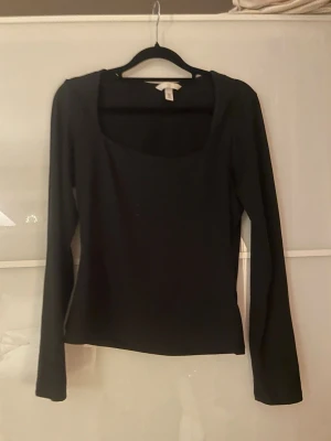 Svart långärmad topp med fyrkantig hals - Säljer en svart långärmad topp från H&M med snygg fyrkantig halsringning. Toppen är slim fit och gjord i mjuk bomull som sitter skönt mot kroppen. Perfekt att styla med jeans eller kjol för en clean look.