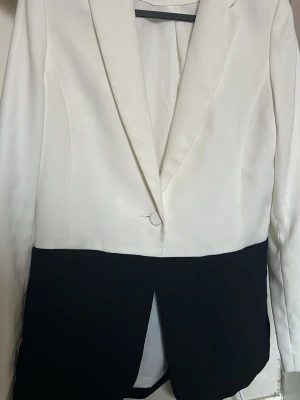 Vit svart kavaj  - Snygg tvåfärgad kavaj i vit och svart. Kavajen har långärmade ärmar med tre vita knappar vid ärmslutet och en stilren, rak passform. Materialet känns slätt och har en elegant look. 