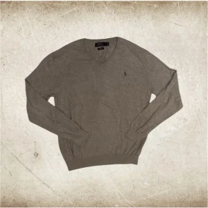 Grå långärmad tröja från Polo Ralph Lauren - Tjena! Säljer nu denna gråa långärmade tröjan från Polo Ralph Lauren i storlek L. Ribbade muddar vid ärmkanterna och vid tröjans slut så den ska hålla sin form så bra som möjligt, och även inte glida runt. Tröjan har en klassisk grå/brun logga broderad på bröstet. En grym tröja för en klassisk everyday-outfit, men även för finare tillfällen. Bara att höra av er om ni skulle ha någon fundering kring något! /Nordic Closet