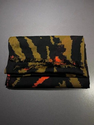 Zara Mönstrad halsduk - Halsduk från Zara med ett unikt camouflage mönster i svart, olivgrön och orange. Materialet är mjukt och lätt, och har fransade kanter. 200x100 cm. Mycket bra skick! Säljs på flera sidor, först till kvarn. 