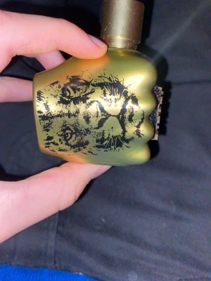 Diesel parfym med lejonmotiv - Cool parfym från Diesel i en guldfärgad flaska formad som en knytnäve med ett lejonmotiv. Perfekt för dig som vill sticka ut och visa attityd. Volym och ingredienser syns ej på bilderna.