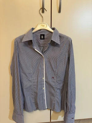 Randig skjorta från Marina Yachting - Snygg skjorta från Marina Yachting med smala blå och vita ränder, klassisk krage och broderad logga på bröstet. Långärmad modell med knappar framtill och diskreta detaljer. Perfekt för dig som gillar stilrena och marina vibbar.