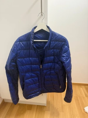 Moncler jacka - Säljer en blå pufferjacka från Moncler med quiltad design och hög krage. Jackan har två sidofickor med dragkedja och Moncler-logga på vänster ärm. Perfekt för dig som vill ha en snygg och lätt jacka med cool vibe. Storlek 3 (M)
