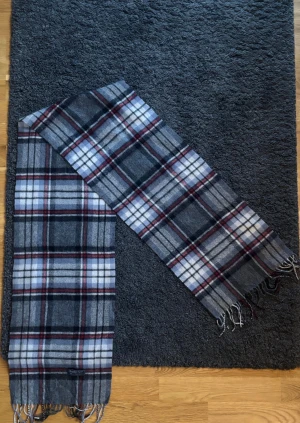 Burberry Halsduk (ÄKTA) - Snygg och mjuk halsduk från Burberry i klassiskt rutigt mönster. Halsduken är lång med tunna fransar i ändarna och passar perfekt till en jacka, kappa eller rock.  Halsduken är varm och skön. Elegant, skönt och sotifistikerat.   ✅ Skick: 8,5/10 🧵Material: Fin ull 🎨 Färg: Grå (men även röd och vit) ✨Tidlös och snygg scarf med fint och välbehandlat material   ‼️Skickas samma dag eller dagen efter köpet genomförs‼️