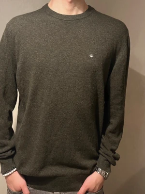 Mörkgrå ulltröja från Junk de Luxe - Snygg mörkgrå tröja från Junk de Luxe i en mjuk och skön blandning av återvunnen italiensk lammull. Tröjan har rund hals, diskret logga på bröstet och långa ärmar. Perfekt för dig som gillar stilrena och klassiska plagg.