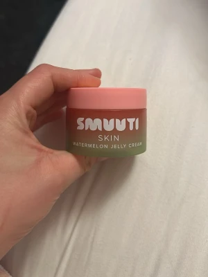 Smuuti Skin Watermelon Jelly Cream - Säljer en Smuuti Skin Watermelon Jelly Cream i en rund burk med rosa lock och grön botten. Krämen har en geléliknande konsistens och doft av vattenmelon. Den är öppna men oanvänd.  
