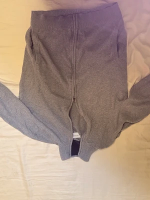 Grå kofta från Pier One med dragkedja - Säljer en stilren grå kofta från Pier One med hel dragkedja framtill. Tröjan har ribbade muddar och krage i mörkblått, samt två fickor på sidorna. Perfekt för lager-på-lager och chill dagar.